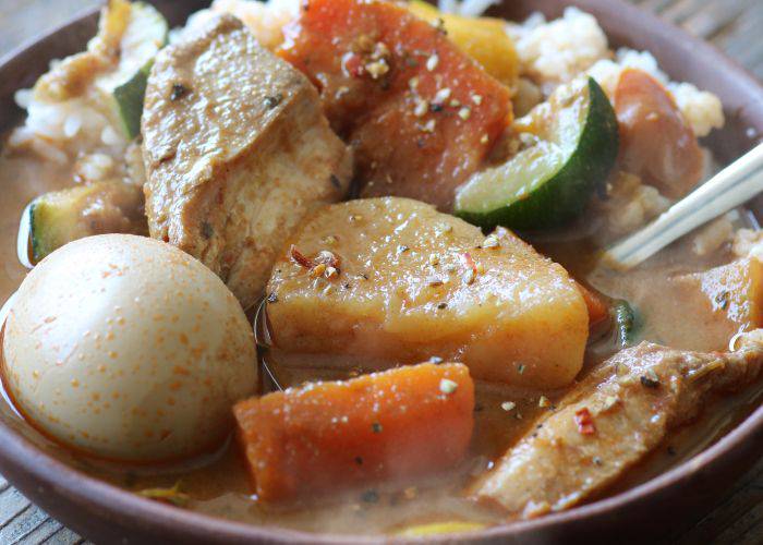 A close-up of a soup curry, featuring meat, potato, vegetables and a soft-boiled egg.